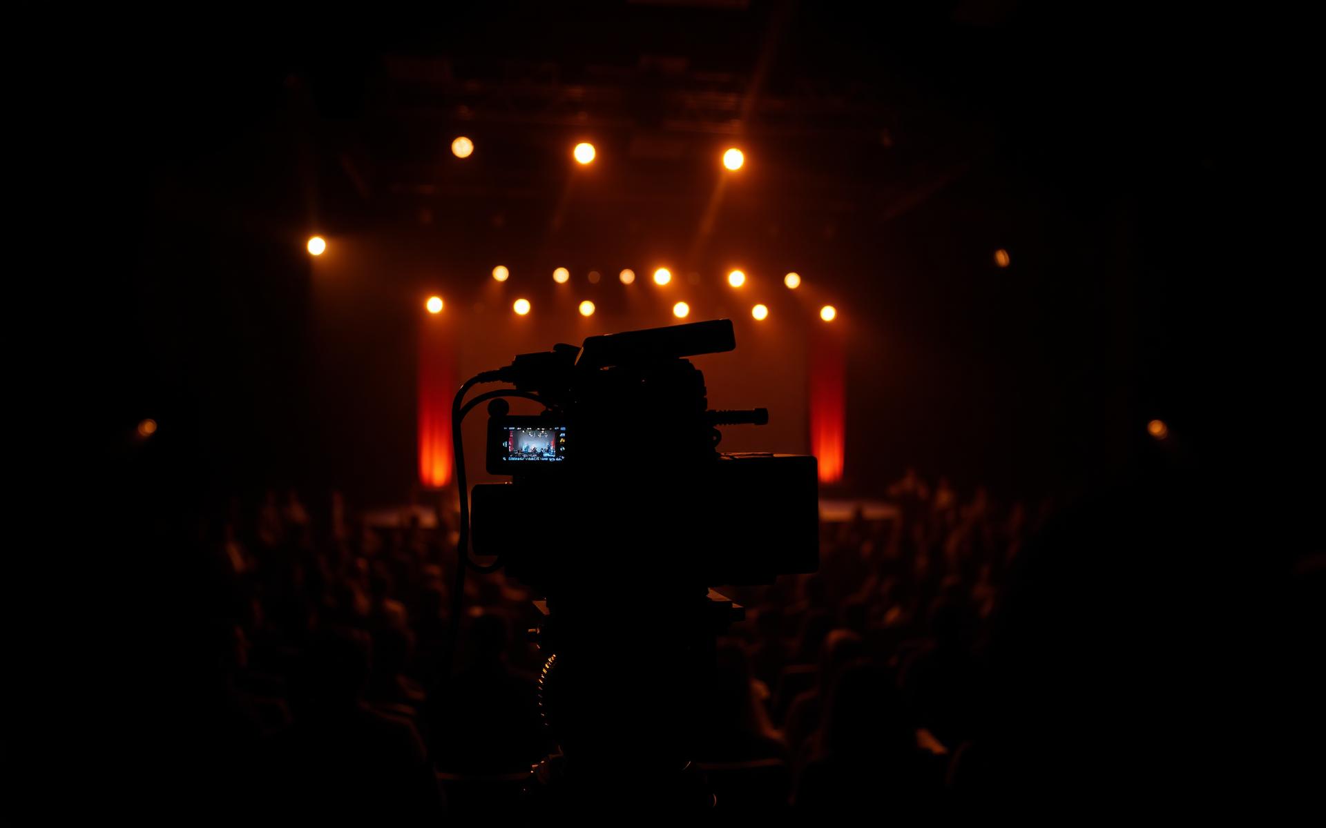 Cinematic view from behind a video camera at a large stage event